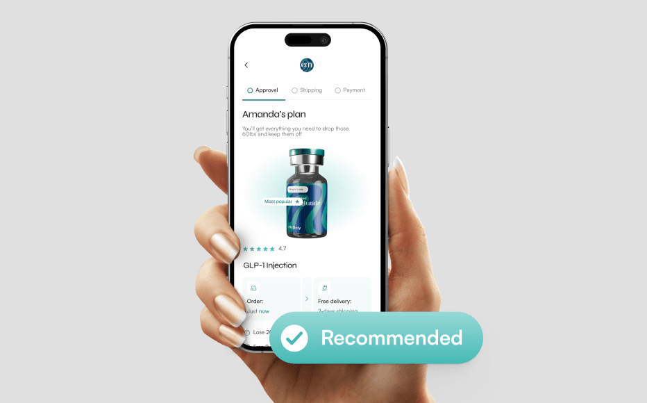 Una mano sosteniendo un teléfono inteligente sobre un fondo gris neutro, mostrando la interfaz de una aplicación móvil de salud. La pantalla muestra un plan personalizado titulado el plan de Amelia para una inyección GLP-1, con un render 3D de un vial médico con un logotipo en tonos verde azulado y azul marino. Sobre el teléfono, un gran botón flotante verde azulado con un ícono de marca de verificación blanca dice Recomendado. El diseño de la interfaz es minimalista, con acentos en verde azulado e incluye indicadores de progreso para Aprobación, Envío y Pago.